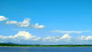 Doorzichtig water Aan de meer met berg heuvel en blauw lucht wit wolk achtergrond in zomer tijd vervallen video