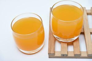 Glass glasses with orange juice on a wooden stand. A soft drink in a glass on a white background. photo