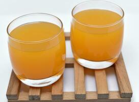 Glass glasses with orange juice on a wooden stand. A soft drink in a glass on a white background. photo