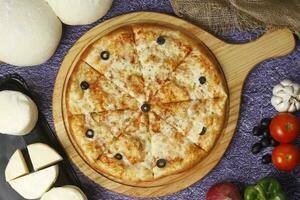 Flatbread pizza garnished with fresh angular on wooden pizza board top view dark stone background photo