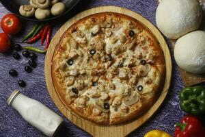 Flatbread pizza garnished with fresh angular on wooden pizza board top view dark stone background photo