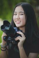 asiático adolescente con dientes sonriente cara y participación dslr cámara en mano foto