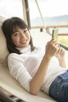 beautiful asian younger woman relaxing  holding smartphone  on cradle photo