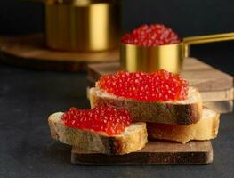 rojo caviar en rebanadas de blanco trigo un pan en un negro mesa, concepto de lujo y gastrónomo cocina foto