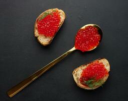 rojo caviar en rebanadas de blanco trigo un pan en un negro mesa, concepto de lujo y gastrónomo cocina foto