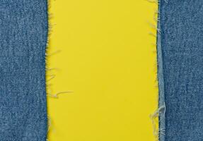 Torn edges of blue jeans on a yellow background photo