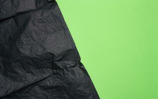 Crumpled sheet of black parchment paper, green background photo