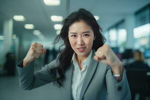 Asian Businesswoman Showing a Fighting Pose, Beautiful Manager Gestures Raising Fists in Modern Office, Female Entrepreneur Fights a Problem, Celebrate Success and Achieving Goals photo