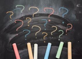 Multicolored crayons on a black chalk board and drawn question marks. Searching of decisions photo