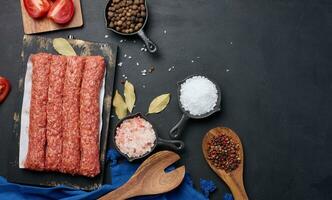 Raw lula kebab sausages on a board and spices, top view photo