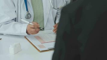 Doctor and patient sitting and talking at medical examination at hospital office, close-up. Therapist filling up medication history records. Medicine and healthcare concept. video