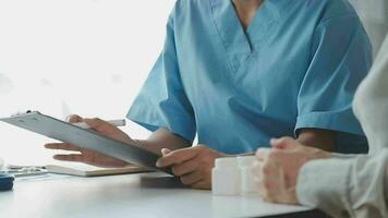 Doctor and patient sitting and talking at medical examination at hospital office, close-up. Therapist filling up medication history records. Medicine and healthcare concept. video