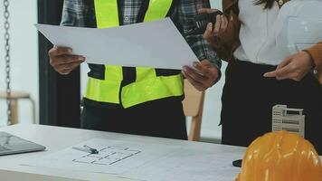 costruzione e struttura concetto di ingegnere o architetto incontro per progetto Lavorando con compagno e ingegneria utensili su modello edificio e planimetria nel Lavorando luogo, contrarre per tutti e due aziende. video