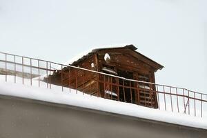 Wooden dovecote or bird house on roof of house with fence. Snowing, winter. Copy space photo