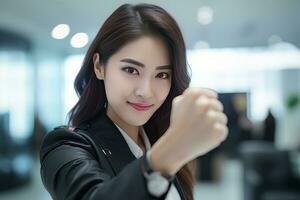 Asian Businesswoman Showing a Fighting Pose, Beautiful Manager Gestures Raising Fists in Modern Office, Female Entrepreneur Fights a Problem, Celebrate Success and Achieving Goals photo