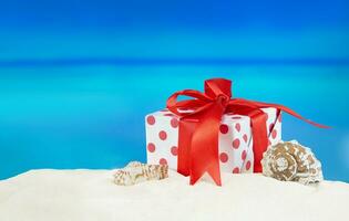 blanco rojo regalo caja con polca puntos con arco en arenoso playa con estrella de mar y concha. venta. Navidad, nuevo año, cumpleaños. Días festivos en caliente países. Copiar espacio foto