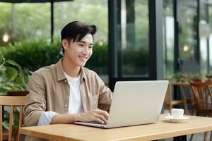 Portrait of Cheerful Male Student Learning Online in Coffee Shop, Young Asian Man Studies with Laptop in Cafe, Doing Homework photo