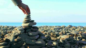 Hand putting last stone on pyramid at the seaside video