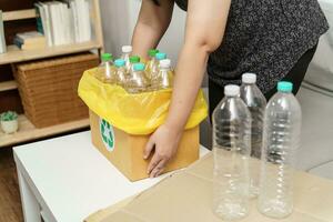 Home recycle eco green zero concept Woman throwing empty plastic bottle in recycling bin with yellow garbage bags at home. photo