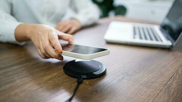 Charging mobile phone battery with wireless charging device in the table. Smartphone charging on a charging pad. Mobile phone near wireless charger Modern lifestyle technology concept. photo