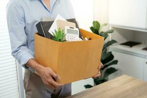 Business man sending resignation letter and packing Stuff Resign Depress or carrying business cardboard box by desk in office. Change of job or fired from company photo