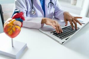 médico consultar paciente en ordenador portátil con anatómico modelo de humano corazón cardiólogo apoyos el corazón en línea médico cita.. foto