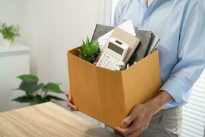 Business man sending resignation letter and packing Stuff Resign Depress or carrying business cardboard box by desk in office. Change of job or fired from company photo