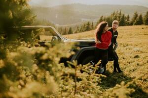 Young couple relaxing by a terrain vehicle hood at countryside photo