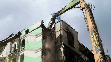 excavador con hidráulico trituradora a el demolición de un residencial edificio. ciudad renovación. desmantelamiento, destrucción de un Alto de muchos pisos edificio para reconstrucción. escombros claro. video