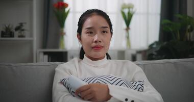 antal fot av Lycklig ung asiatisk kvinna tittar på en film på tv medan Sammanträde på de soffa i de levande rum. wellness på Hem, avkopplande och livsstil begrepp. video