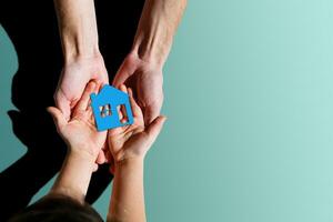 people, charity, family and home concept - close up of woman and girl holding paper house cutout in cupped hands photo