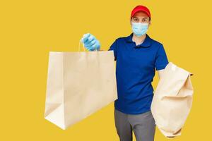 Delivery man in mask and gloves bring fresh food to customer's home. Stay home. Online shopping concept. yellow background photo