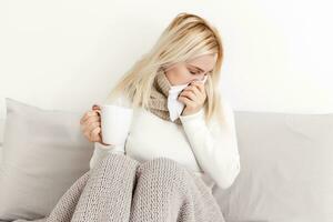 Sneezing and blowing her nose, a young woman struggles with a head cold photo