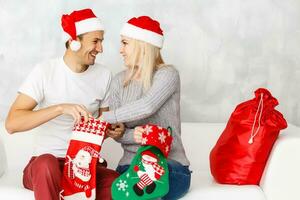 Pareja alegre cara cheque fuera regalo en Navidad calcetín. mujer y hombre en Papa Noel sombrero esperando regalo antecedentes. cheque contenido de Navidad media Navidad concepto. foto