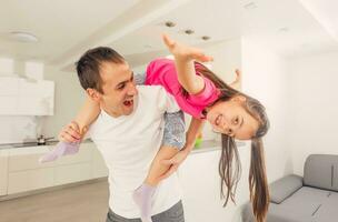 Little daughter and her handsome young dad are playing together in room. Girl is holding a toy plane and dad is holding his daughter photo