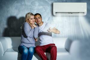 couple turning on air conditioner during the summer heat while sitting on sofa photo