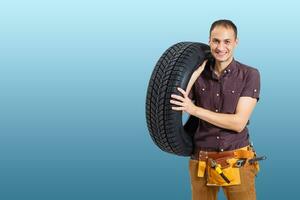 coche mecánico que lleva neumático en azul antecedentes. contento hombre sonriente amd mirando dentro cámara foto
