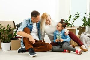 contento familia sentado en de madera piso. padre, madre y niño teniendo divertido juntos. Moviente casa día, nuevo hogar y diseño interior concepto foto