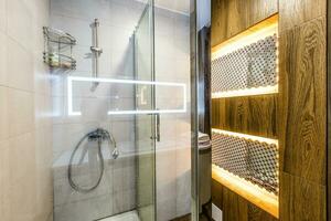 Big and stylish bathroom in brown and beige colors, big mirror on wall, sink and bowl. Shower cabin with glasses wall. photo