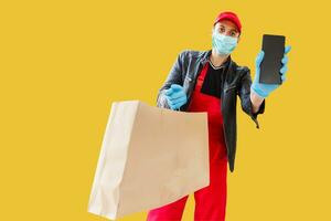 Delivery man in mask and gloves bring fresh food to customer's home. Stay home. Online shopping concept. yellow background photo