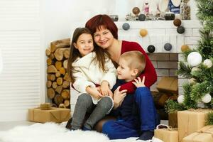 Family on Christmas eve at fireplace. Mother and little kids opening Xmas presents. Children with gift boxes. Living room with traditional fire place and decorated tree. Cozy winter evening at home. photo