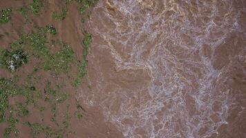 La vista aérea del agua liberada del canal de drenaje de la presa de hormigón es una forma de desbordamiento de agua en la temporada de lluvias. vista superior de los flujos de agua turbia del bosque marrón de una presa en tailandia. video