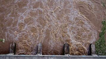 antenne visie van water vrijgelaten van de afvoer kanaal van de beton dam is een manier van overlopend water in de regenachtig seizoen. top visie van troebel bruin Woud water stromen van een dam in Thailand. video