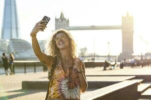 Reino Unido, Londres, sonriente joven mujer tomando un selfie con torre puente en antecedentes foto