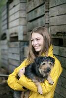 Smiling woman on a farm standing at wooden boxes holding dog photo