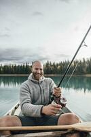 Canada, British Columbia, portrait of happy man fishing in canoe on Boya Lake photo