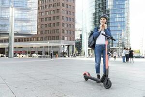 Woman with e-scooter in the city putting on helmet, Berlin, Germany photo