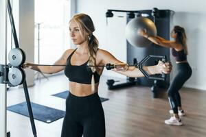 Young female athlete using rowing machine and other sportswoman doing exercise with fitness ball photo