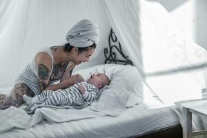 Tattooed young woman with her baby in canopy bed photo