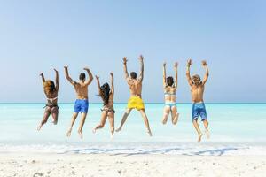 grupo de amigos a el playa, saltando para alegría foto